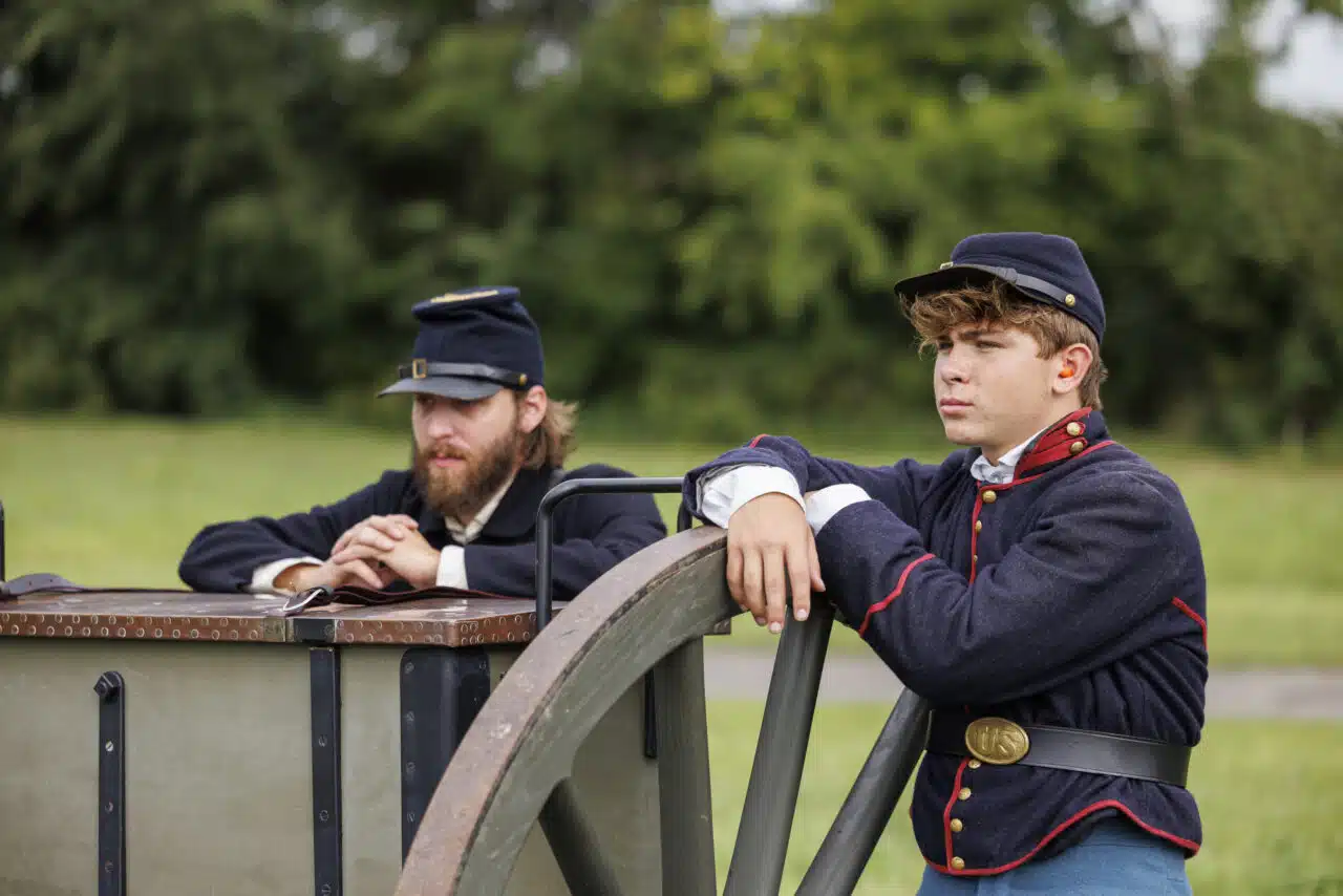 Battle of Richmond Reenactment - Two men looking from behind the cannon