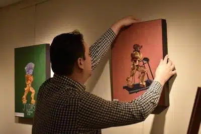 Randy Westbrook straightening artwork on the wall of the Richmond Area Arts Center