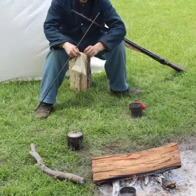 Reenactor sitting by fire reworking weapon